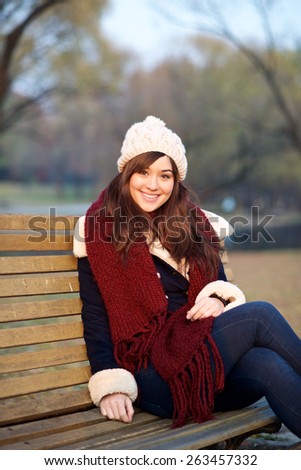 Young girl sitting on bench in a park in the Winter looking at camera