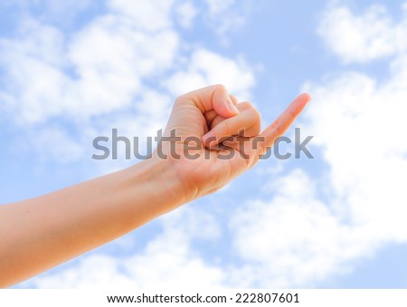 A pinkie and  hand reaching toward the blue sky  background.