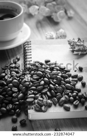Coffee bean with cup coffee and notebook on old wooden table black and white color tone