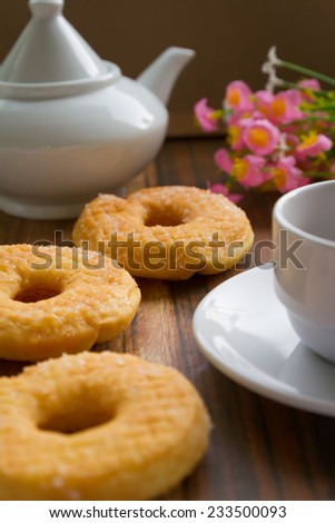three  delicious sugared ring donuts served on white plate with a cup of hot drink on the side.