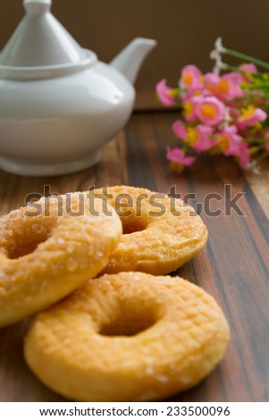 three  delicious sugared ring donuts served on white plate with a jar of hot drink on the side.