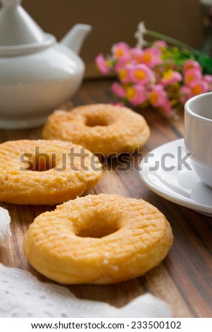 three  delicious sugared ring donuts served on white plate with a cup of hot drink on the side.