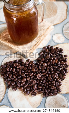 A glass of black iced coffee surrounded by coffee beans.