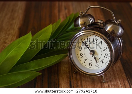 Old fashioned alarm clock with leapf on wood table  background