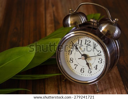 Old fashioned alarm clock with leapf on wood table  background