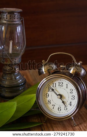 Old fashioned alarm clock and old lamp with leapf on wood table  background