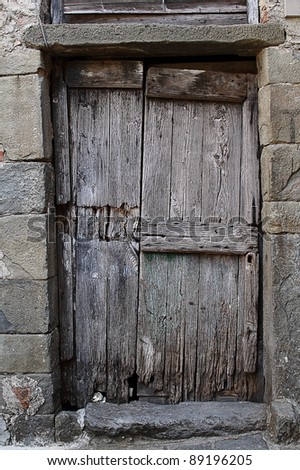 Old wooden door in a gray masonry wall, Italy