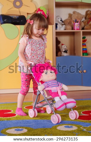 Child in the nursery playing toy doll in a stroller