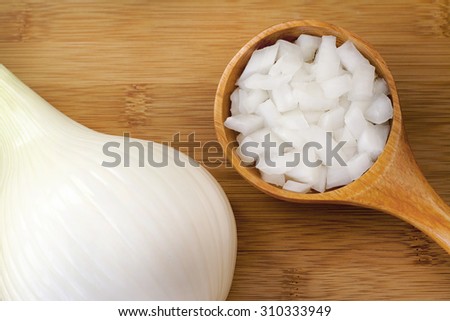 Diced chopped onion in a wooden spoon placed on a chopping board next to a large onion cut in half , room for text and copy space