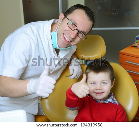 little boy in a red sweater went to the dentist in the dental chair sits next to a doctor to do the dentist to see if his teeth were okay / little boy at the dentist