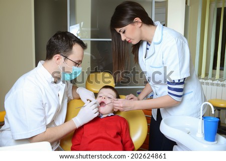 little boy in a red sweater went to the dentist in the dental chair sits next to a doctor to do the dentist to see if his teeth were okay/little boy in a red sweater went to the dentist