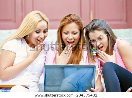 happy young high-school students or college girls sitting on the steps outside the school loud laugh and a break from school with a laptop in the hands/happy young high-school students