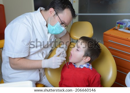little boy in a red sweater went to the dentist in the dental chair sits next to a doctor to do the dentist to see if his teeth were okay/little boy in a red sweater went to the dentis