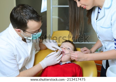 little boy in a red sweater went to the dentist in the dental chair sits next to a doctor to do the dentist to see if his teeth were okay/went to the dentist