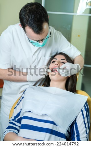 young women to the dentist in the dental chair sits next to a doctor to do the dentist to see if his teeth were okay/young women to the dentist
