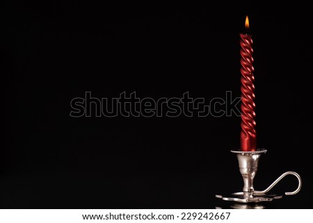 silver candlestick with one burning red candle in front of black background/silver candlestick