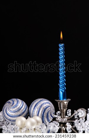 silver candlestick with one blue candle and glass balls stands next to a multitude of crystal stones on the mirror/silver candlestick with one blue candle