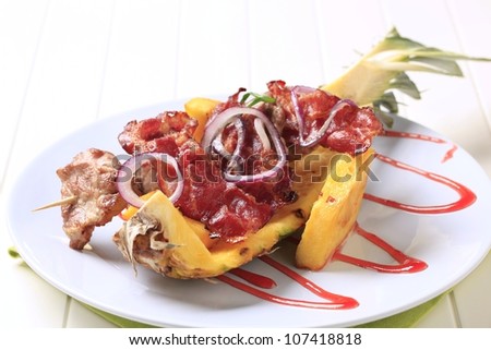 Meat skewers and crispy bacon strips on pineapple