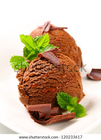 Two scoops of chocolate ice cream decorated with mint leaves and chocolate curls