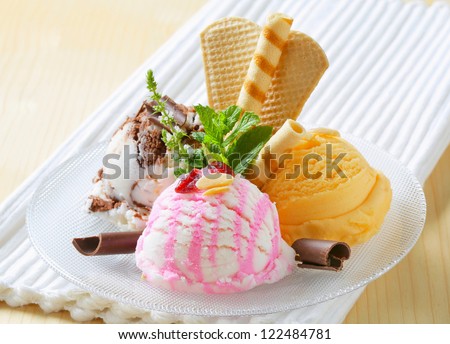Three scoops of ice cream garnished with wafers and herbs