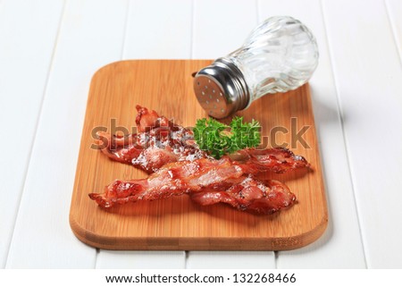 crispy fried bacon with salt cellar on a wooden cutting board