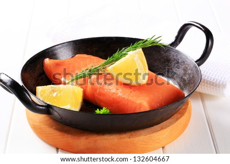 fresh salmon steak with herbs and lemon, in a iron pan