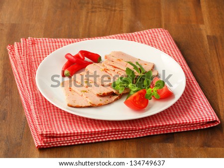 sliced leberkase with tomatoes and chili pepper on a round plate