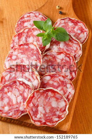 full frame with sliced french salami with decorated with fresh herbs, on a wooden cutting board