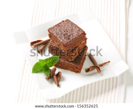 three pieces of smooth brownies with chocolate curls on a square plate