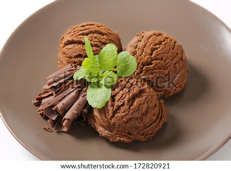 three chocolate ice cream scoops with chocolate flakes and herbs, served on a plate