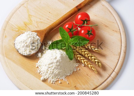 overhead view of soft wheat flour with wheat ear, wooden spoon and fresh tomatoes, on the wooden cutting board