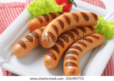 detail of grilled hot dog sausages with lettuce and tomato on paper plate