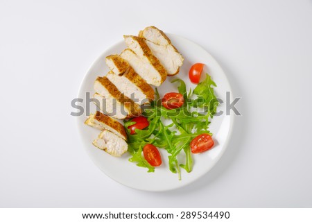 plate of sliced chicken breasts with rucola and cherry tomatoes on white background