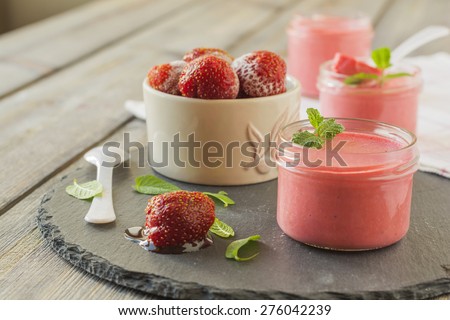 Strawberry mousse in glass jars and frozen strawberries on an old wooden table background.Selective focus.