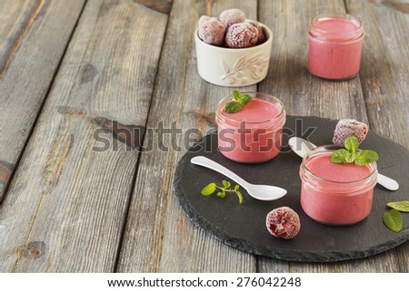 Strawberry mousse in glass jars and frozen strawberries on an old wooden table background.Selective focus.