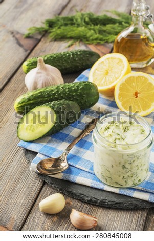 Fresh tzatziki in glass jar with cucumber, lemon,garlic and olive oil on an old wooden table background.Selective focus.