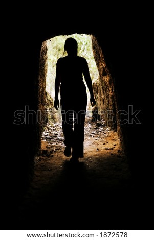 Looking towards the entrance of a cave with a woman walking forwards
