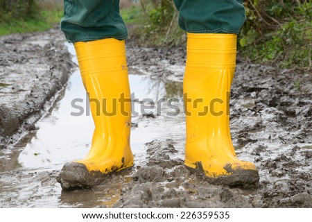 Human leg with Yellow Muddy rubber boots on wet silt