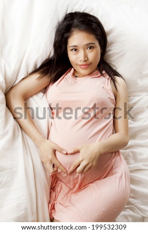 Pregnant woman forming a symbol of love with hands on the mattress