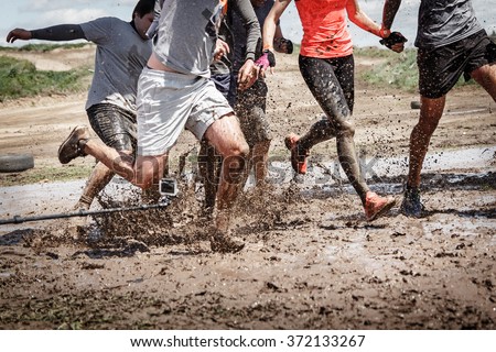 Team competition with an obstacle. Finish team in a big mud puddle. Close-up