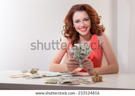young girl at  table with greedy counts  money lying on  table and looking at  camera