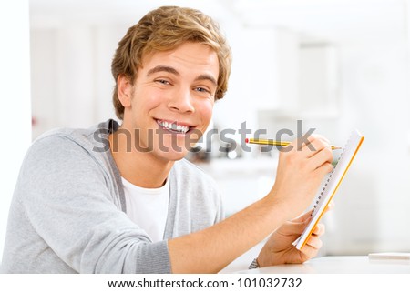 Happy young male student doing homework and studying in study at
