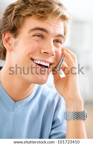Joyful young man using mobile phone at home is happy and smiling