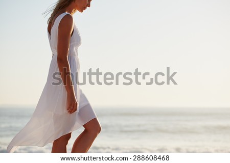 Beautiful woman wearing white flowing dress walking on beach