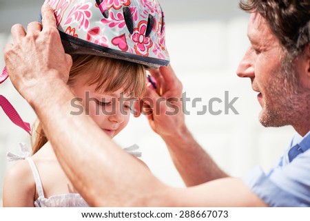 Father teaching brave daughter to ride bicycle putting on safety helmet