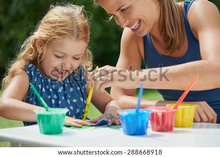 Mother and daughter painting with hands outdoors showing emotional connection