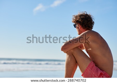 Attractive young man with healthy body sitting on the beach looking out at sea view