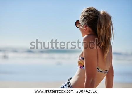 Close up portrait of unrecognizable sexy woman from behind tanning and looking towards the ocean is wearing floral bikini