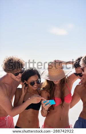 Attractive young mixed race group of friends looking at mobile phone wearing bikinis and swim shorts with athletic bodies