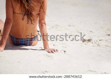 Hot girl with perfect body and sexy bum sitting on sandy beach in a bikini